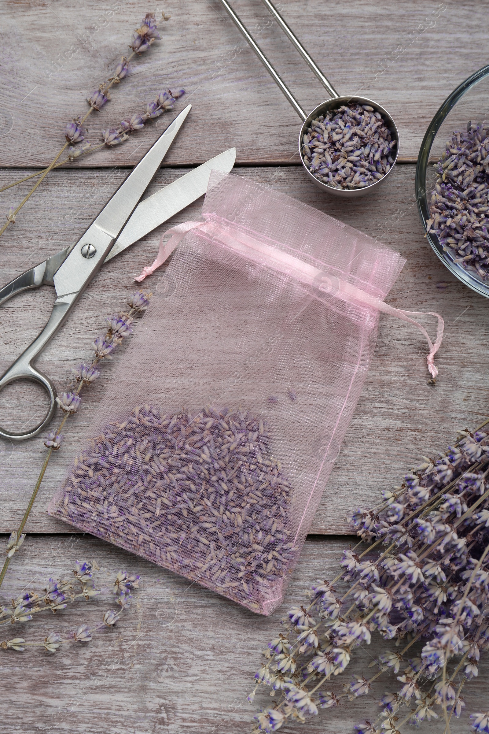 Photo of Scented sachet with dried lavender flowers and scissors on wooden table, flat lay