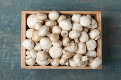 Photo of Wooden crate full of fresh raw mushrooms on table, top view