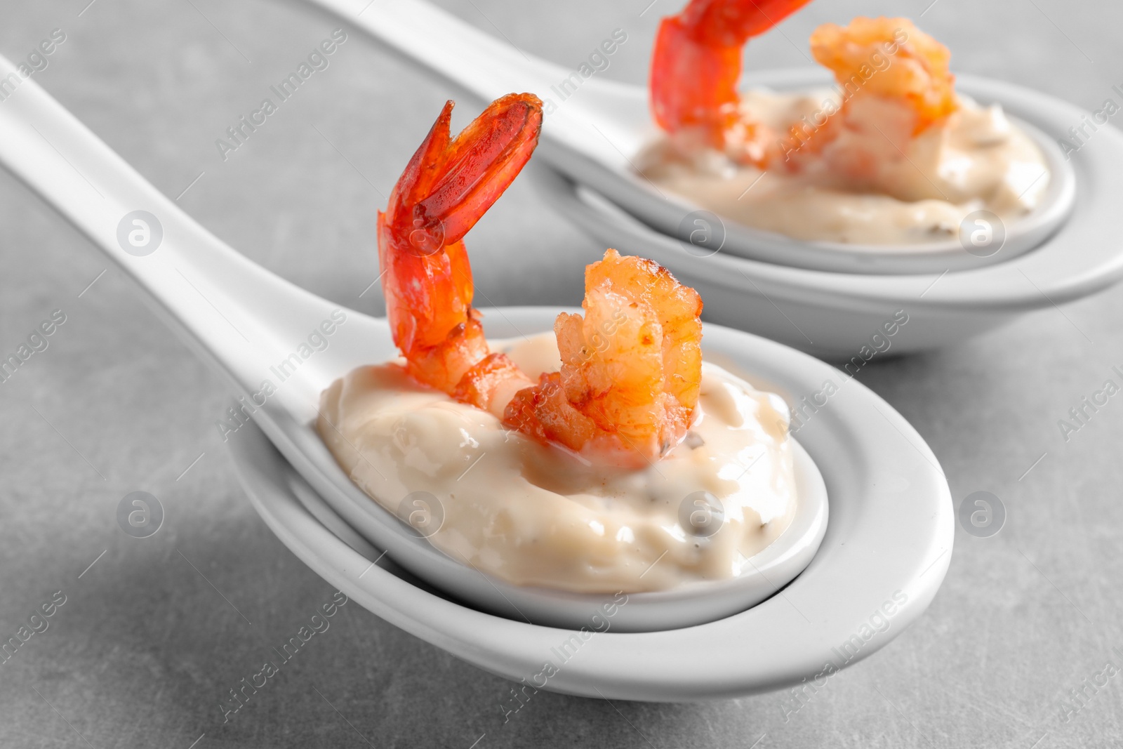 Photo of Delicious snacks with shrimp in spoons on grey background