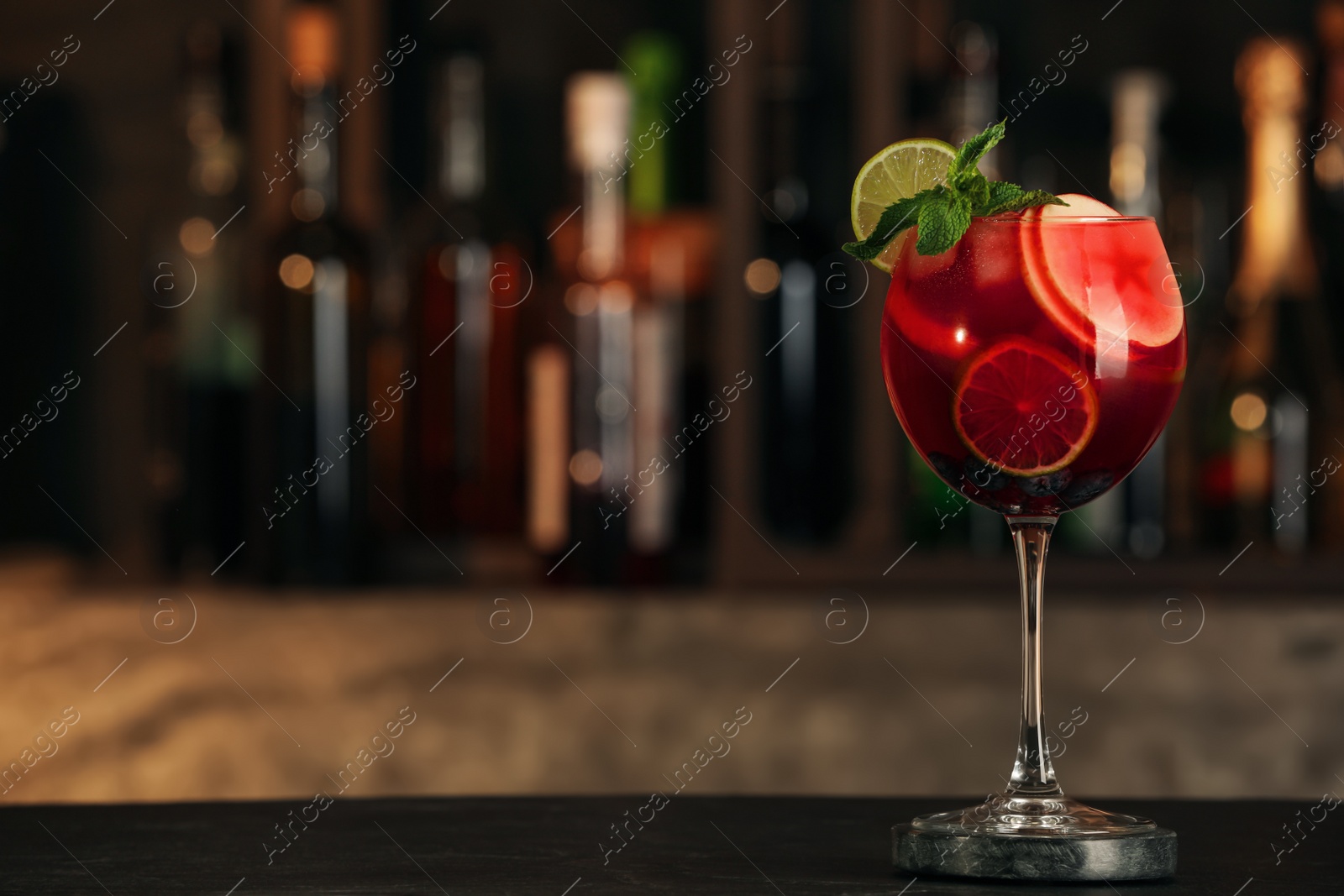 Photo of Delicious sangria cocktail on black table in bar. Space for text