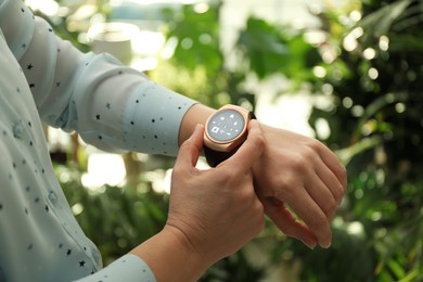 Woman setting smart home control system via smartwatch outdoors, closeup. App interface with icons on display