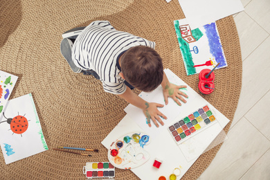 Little child painting on floor at home, top view