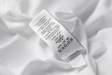 Photo of Clothing label with recommendations for care on white garment, closeup