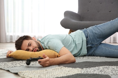 Photo of Lazy young man playing video game while lying on floor at home