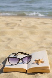 Beautiful sunglasses, book and starfish on sand near sea