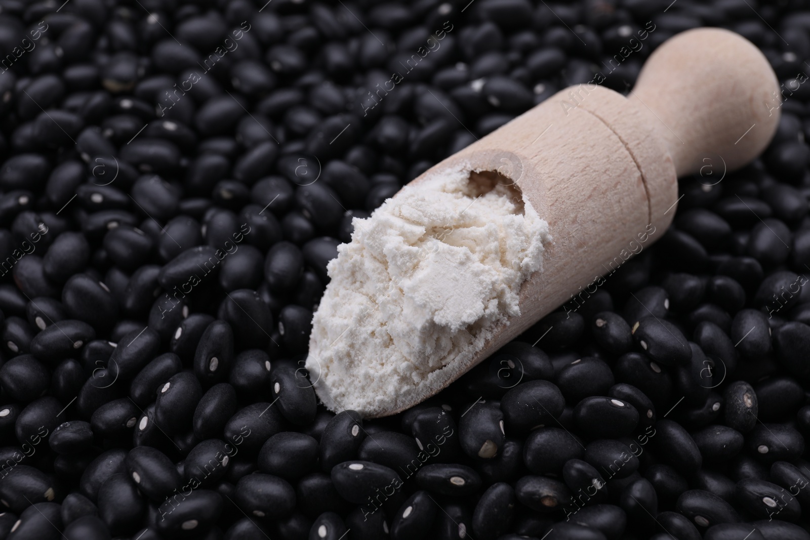 Photo of Wooden scoop with flour on black kidney beans, closeup. Space for text