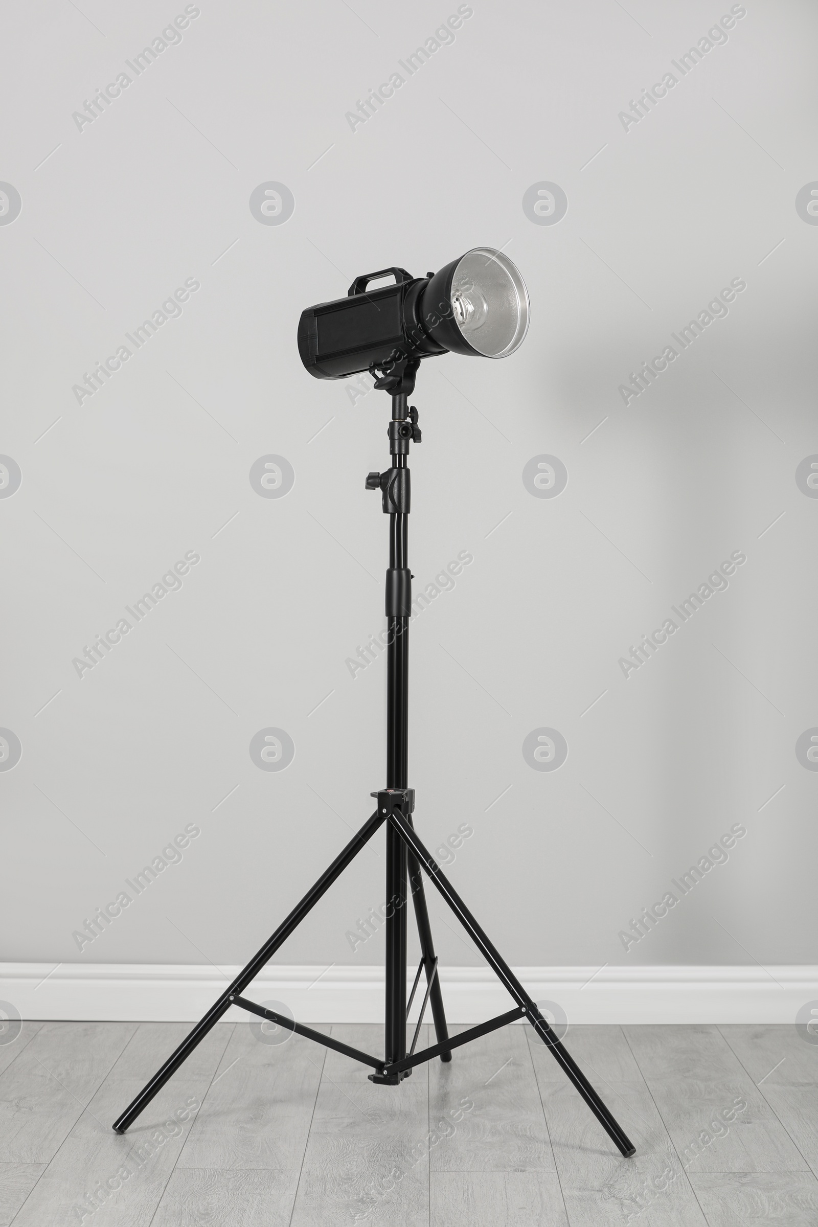 Photo of Professional beauty dish reflector on tripod near grey wall in room. Photography equipment