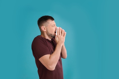 Man suffering from allergy on blue background. Space for text