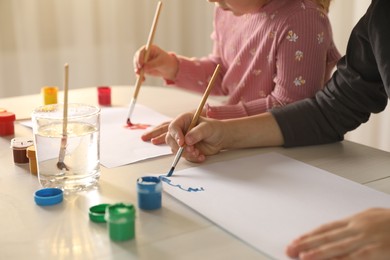 Photo of Little children drawing with brushes at wooden table indoors, closeup