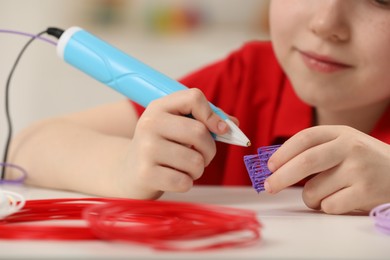 Photo of Boy drawing with stylish 3D pen at white table, closeup