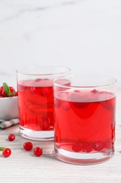 Photo of Tasty cranberry juice in glasses and fresh berries on white wooden table
