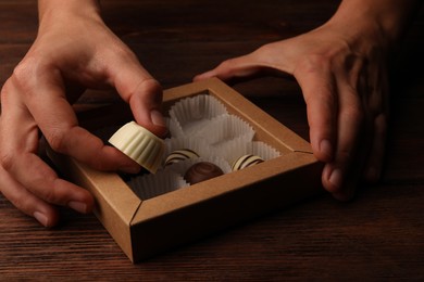 Photo of Woman taking chocolate candy out from box at wooden table, closeup