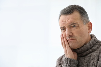 Photo of Mature man suffering from strong tooth pain on light background, space for text