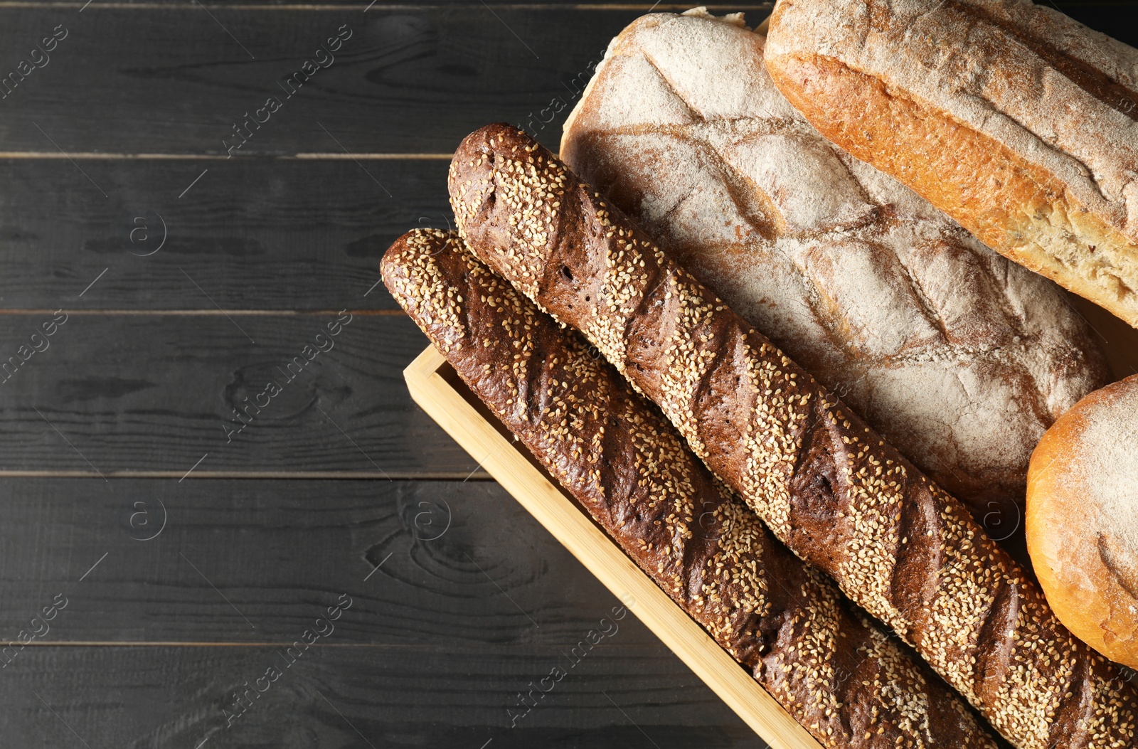 Photo of Basket with different types of fresh bread on black wooden table, top view. Space for text