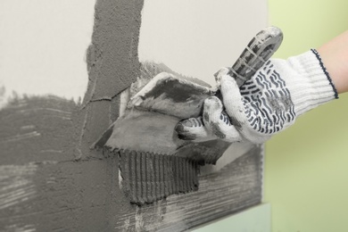 Photo of Worker spreading concrete on wall with spatula, closeup. Tile installation