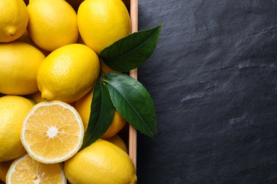 Photo of Many fresh ripe lemons with green leaves on black table, top view. Space for text