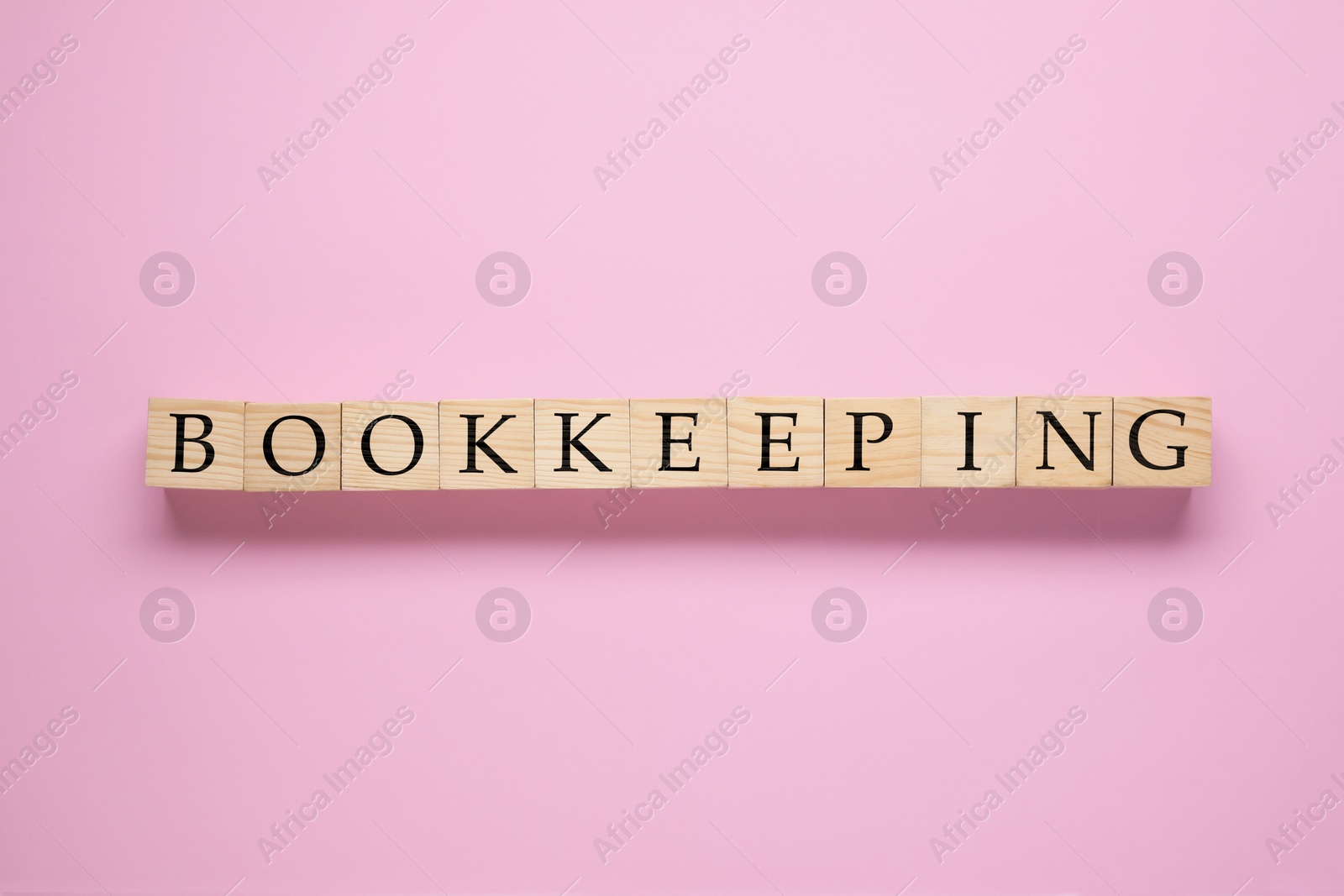 Photo of Word Bookkeeping made with wooden cubes on pink background, top view