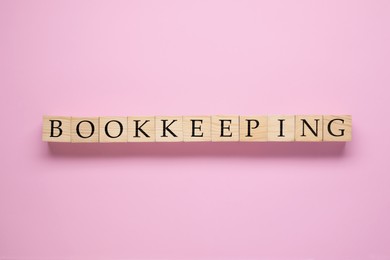 Photo of Word Bookkeeping made with wooden cubes on pink background, top view