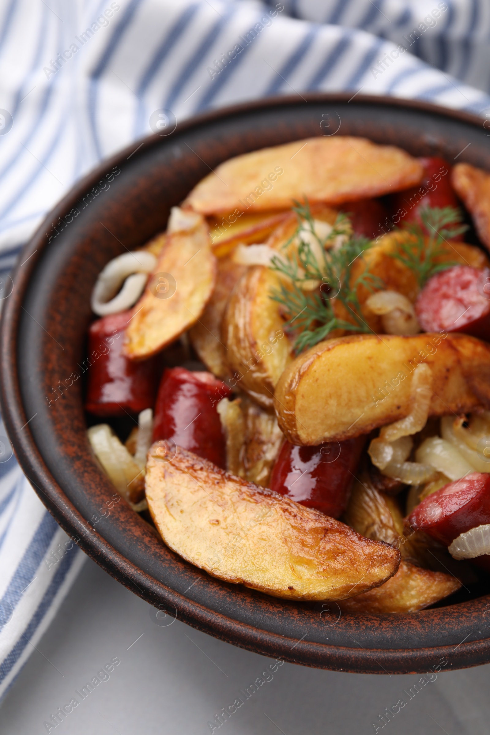 Photo of Delicious baked potato with thin dry smoked sausages, onion and dill in bowl on white table, closeup