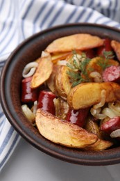 Photo of Delicious baked potato with thin dry smoked sausages, onion and dill in bowl on white table, closeup