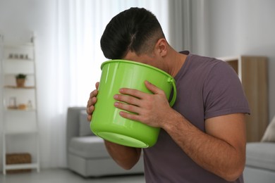 Photo of Man with bucket suffering from nausea at home. Food poisoning