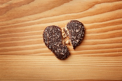 Photo of Broken heart shaped cookie on wooden background, top view. Relationship problems