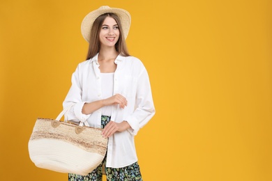 Photo of Beautiful young woman with stylish straw bag on yellow background. Space for text