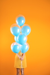 Photo of Young woman hiding behind air balloons on color background