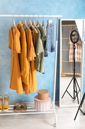 Rack with stylish clothes and mirror near light blue wall indoors