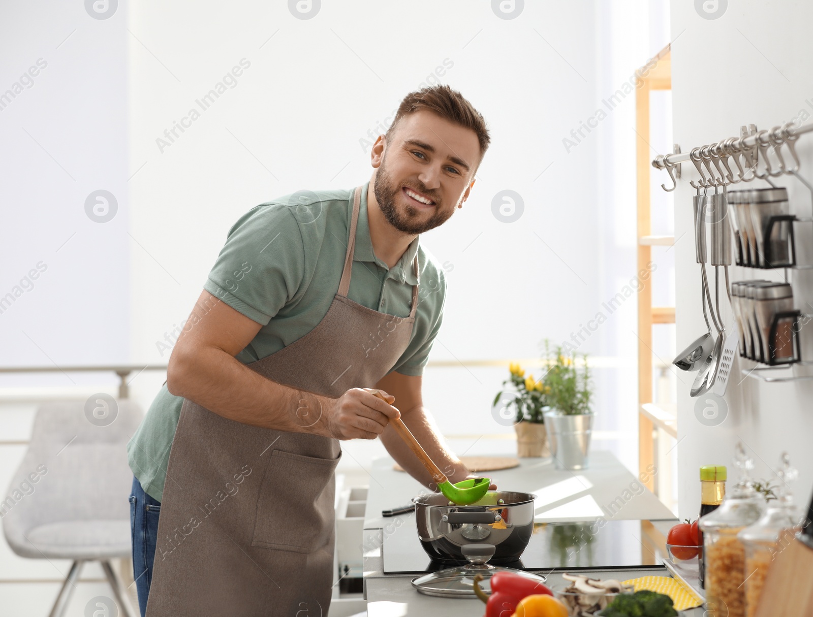 Photo of Young man cooking delicious soup in kitchen