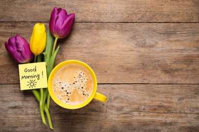 Photo of Delicious coffee, flowers and card with GOOD MORNING wish on wooden table, flat lay. Space for text