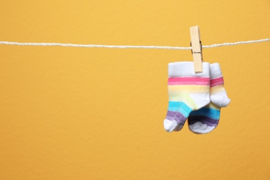 Photo of Cute socks for baby on laundry line against color background. Space for text