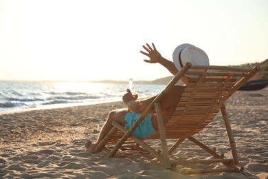 Young man relaxing in deck chair on beach near sea