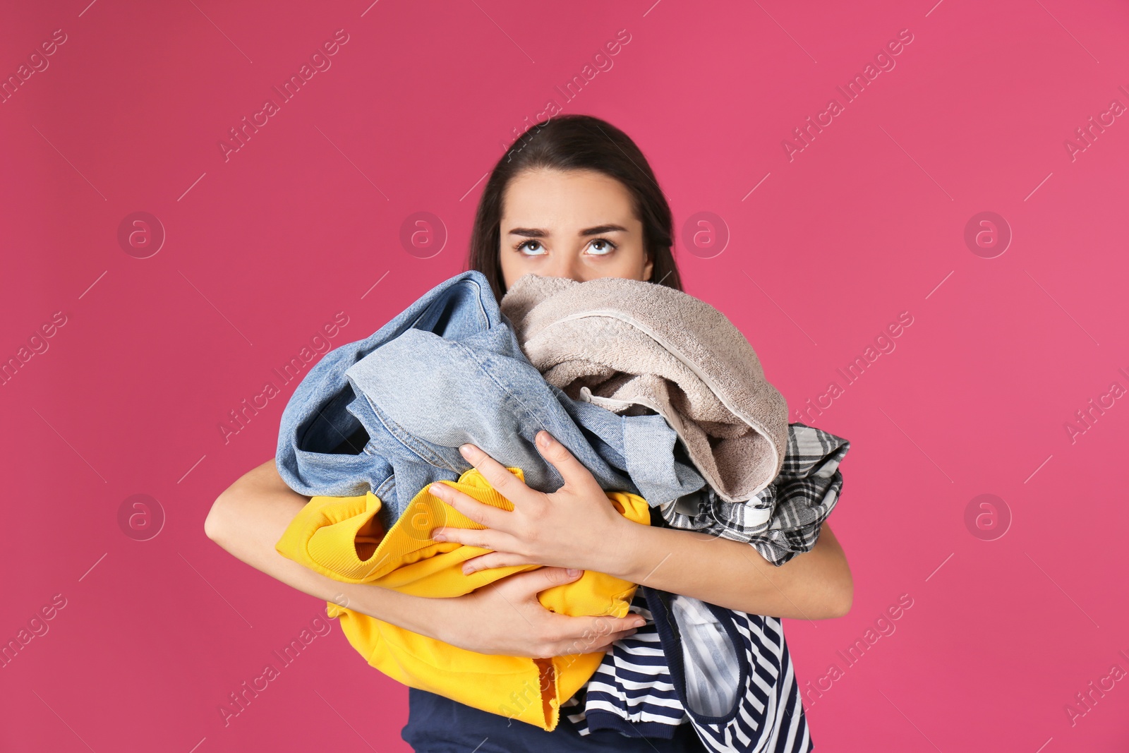 Photo of Young woman holding pile of dirty laundry on color background