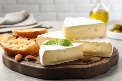 Photo of Tasty brie cheese with basil, bread and almonds on wooden board