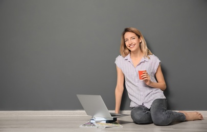 Young blogger with laptop sitting on floor near color wall