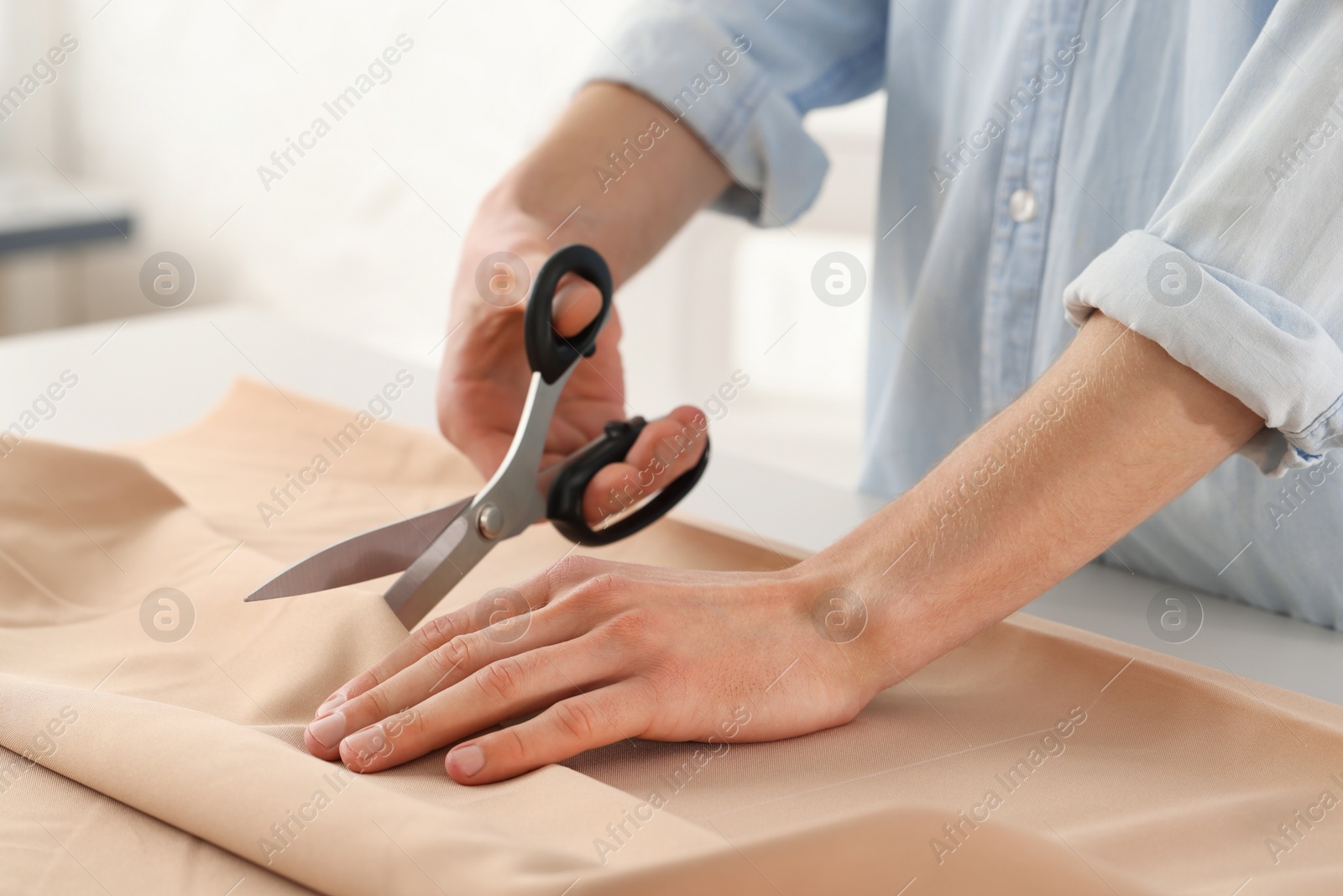 Photo of Dressmaker cutting fabric with scissors at table in atelier, closeup