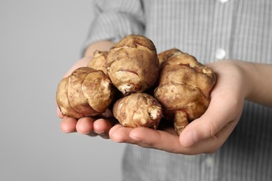 Photo of Woman holding Jerusalem artichokes on light grey background, closeup