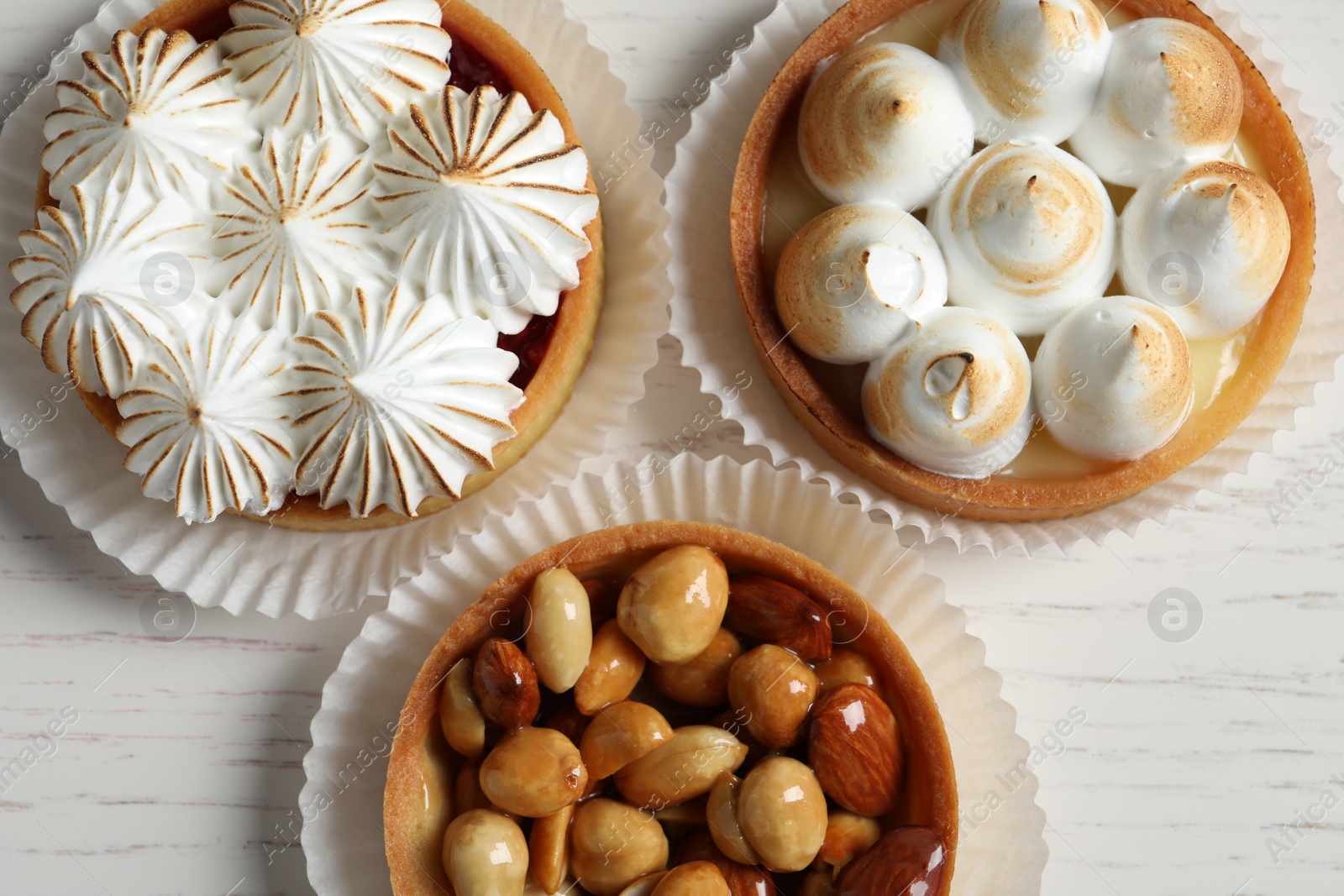 Photo of Different tartlets on white wooden table, flat lay. Tasty dessert