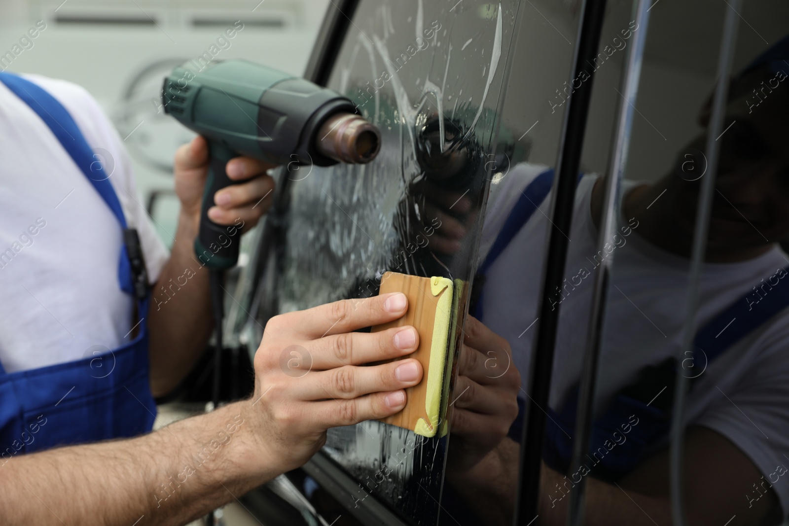 Photo of Worker tinting car window with foil in workshop, closeup