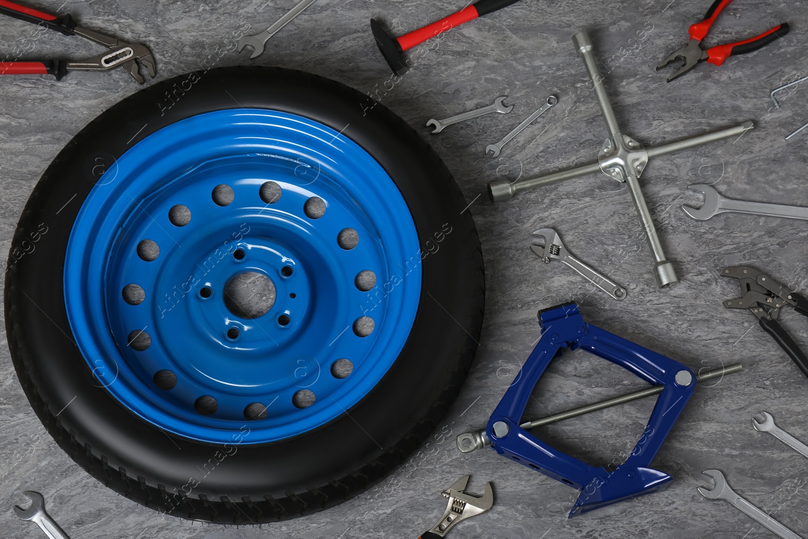 Photo of Car wheel, scissor jack and different tools on grey surface, above view