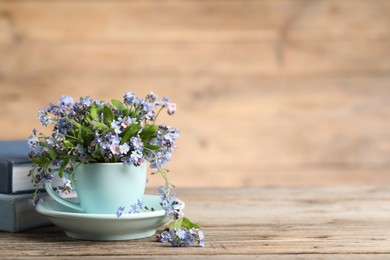 Photo of Beautiful forget-me-not flowers in cup and saucer on wooden table, closeup. Space for text