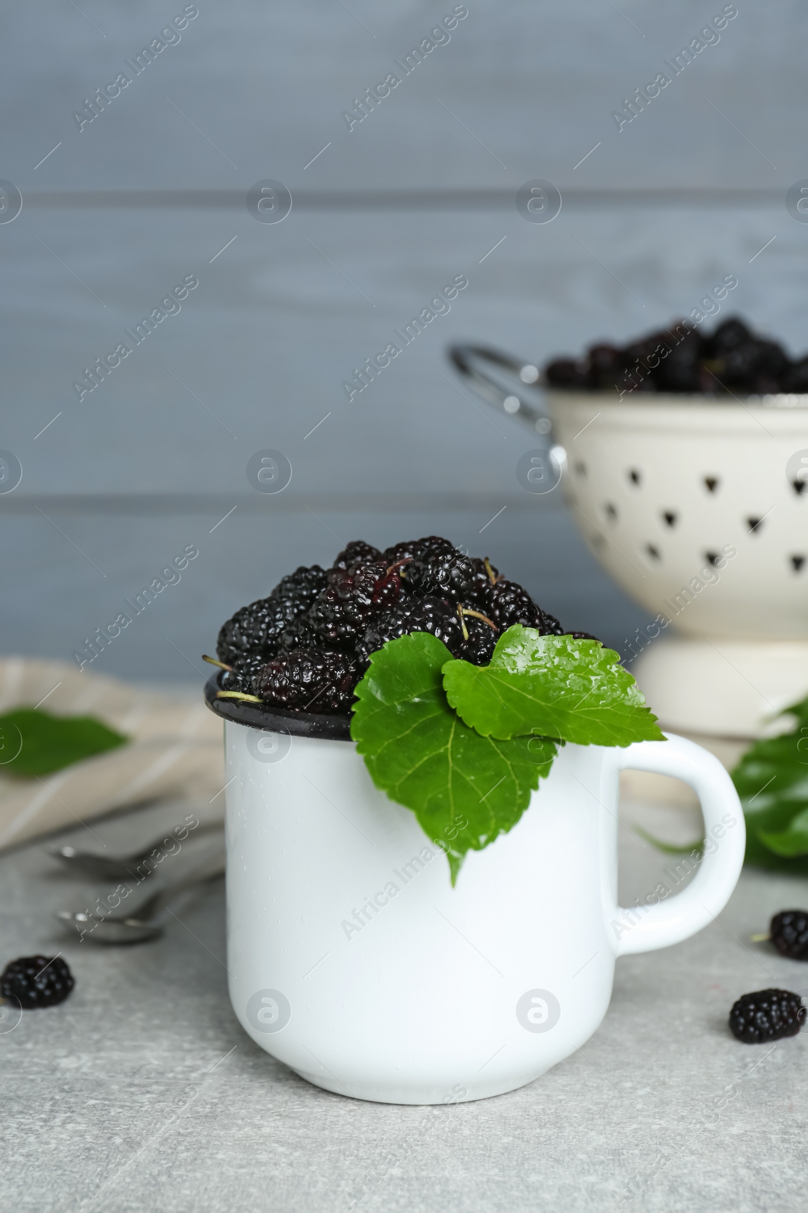 Photo of Cup of delicious ripe black mulberries on grey table