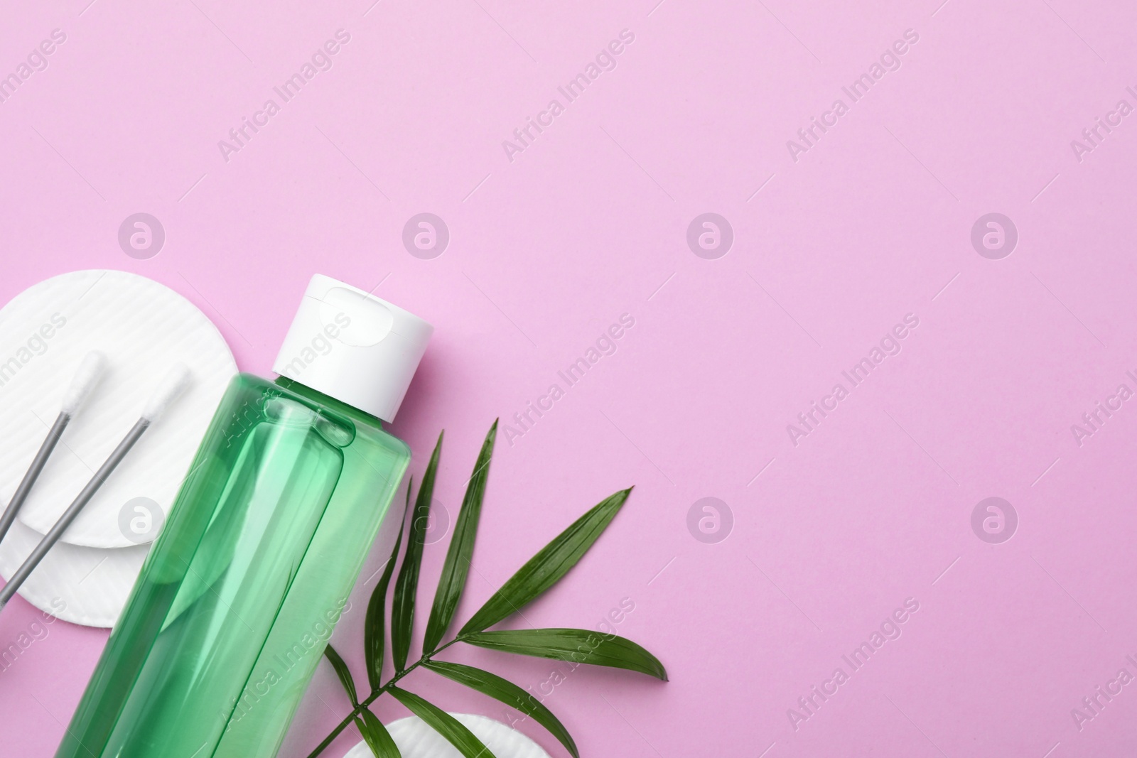 Photo of Bottle of micellar water, twig, cotton pads and swabs on pink background, flat lay. Space for text