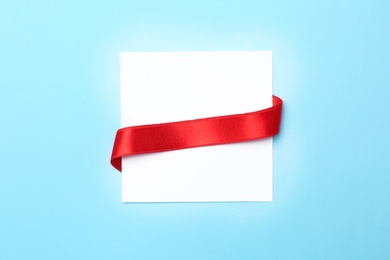 Blank gift tag with satin ribbon on color background, top view