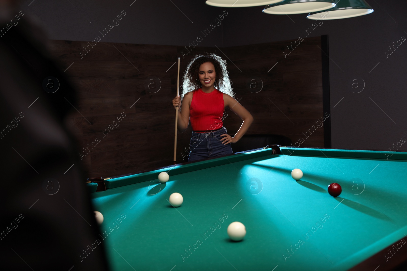 Photo of Young African-American woman with cue near billiard table indoors