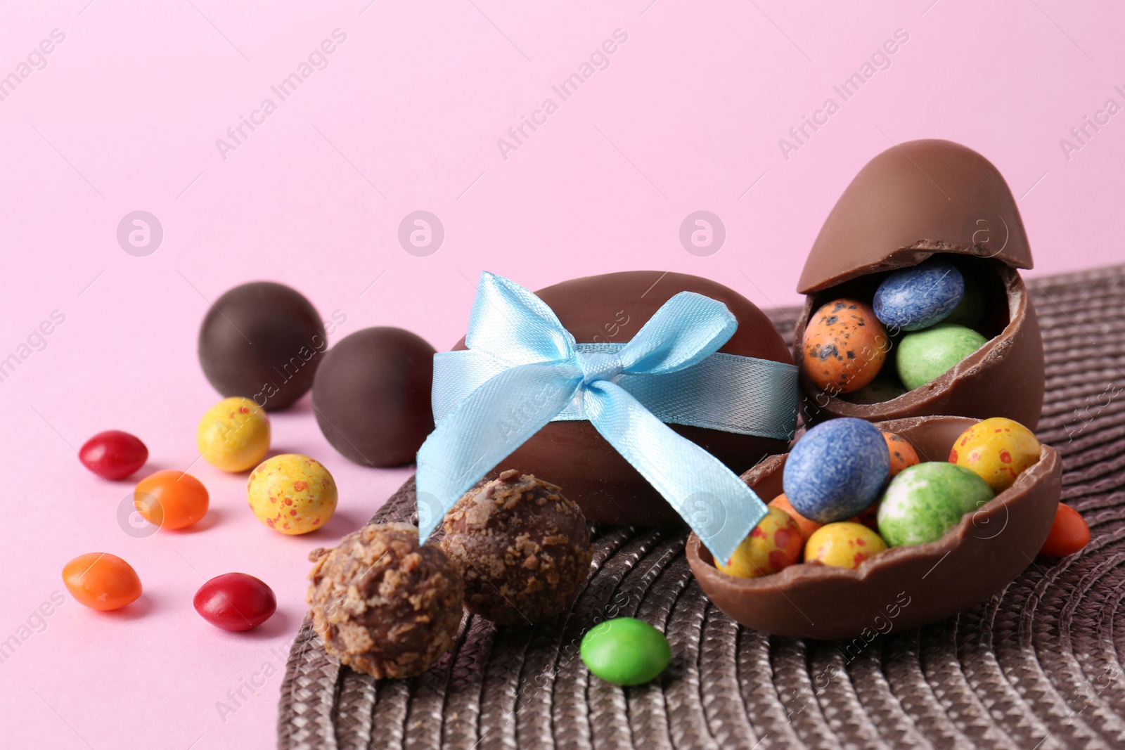 Photo of Tasty chocolate eggs and candies on pink background. Space for text