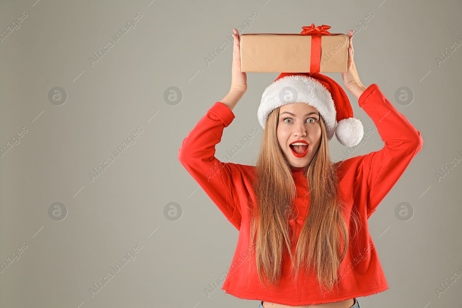 Photo of Young beautiful woman in Santa hat with gift box on grey background. Christmas celebration