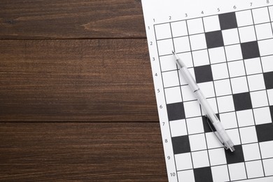 Photo of Blank crossword and pen on wooden table, top view. Space for text