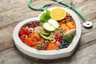 Photo of Heart shaped tray with healthy products and stethoscope on wooden background